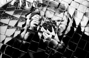 Black and white photo of a man photographing himself in the shiny construction