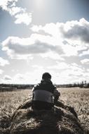 male person sits on hay stack in countryside at fall