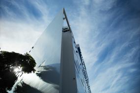 Low angle shot of the modern, shiny, glass building, near the trees, at blue sky with white clouds on background
