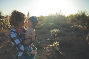 Mom with children in her arms near the plants in the background of sunlight
