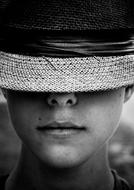 Black and white portrait of a boy with covered eyes in a hat