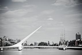 Black and white landscape with the beautiful bridge, above the water, among the building, under the sky with clouds