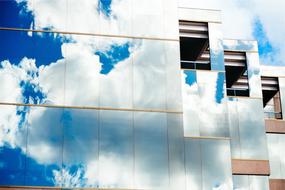 white clouds are reflected in the glass facade of a modern building