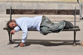 homeless man is sleeping on a park bench