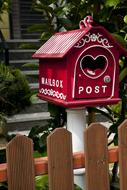 red letter box with letters near the wooden fence