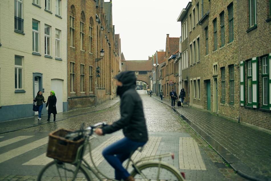 A cyclist in a black jacket rides along a pedestrian crossing among the buildings