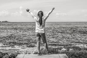 monochrome photo of a girl with hands up on the seashore