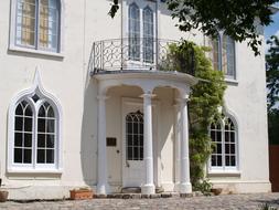 Beautiful balcony of the house, with white columns and green plants, in sunlight