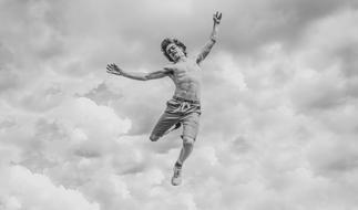 Black and white photo of a jumping young man with bare chest on a background of clouds