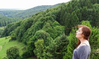 girl with closed eyes stands on top of a hill