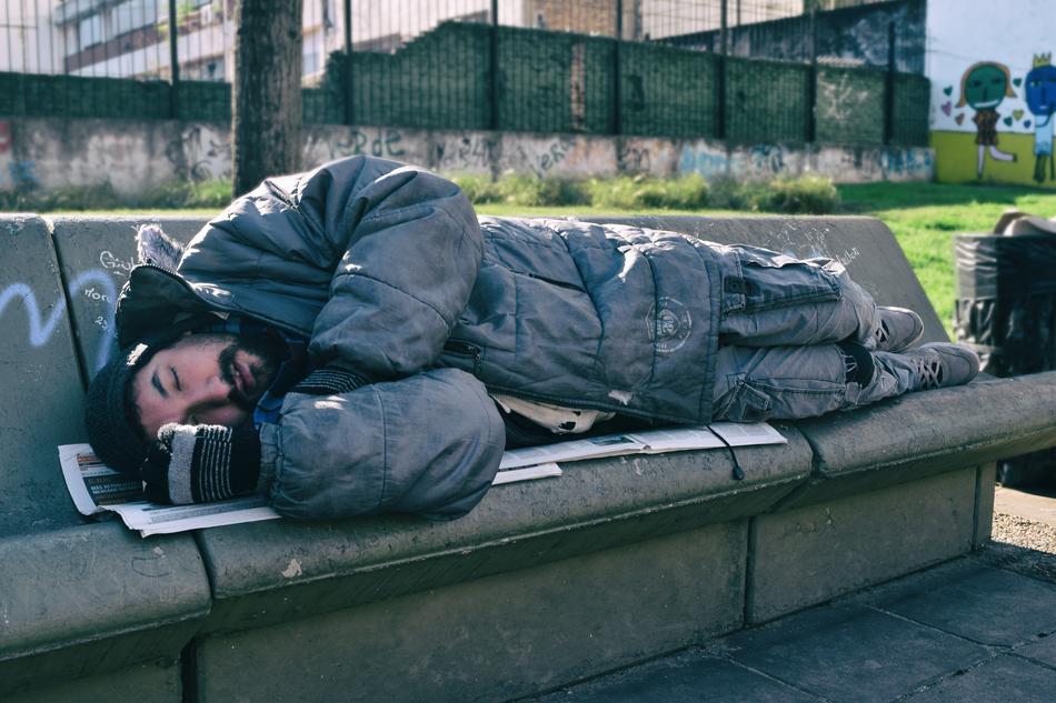 Indigent Man sleep on a stone bench