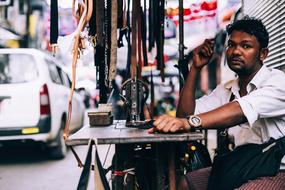 dark skin men sits at table with belts, Vendor