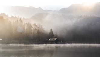 Beautiful, foggy landscape with the house, on the shore of the lake, near the trees, on the mountains, at colorful and beautiful sunset