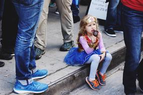 cute Child girl eating Ice cream sits on steps in crowd