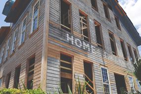 Old and colorful, wooden building, with the "HOME" sign, among the colorful plants, in sunlight
