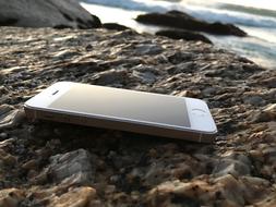 Beautiful, shiny, white Iphone on the colorful stones, near the water