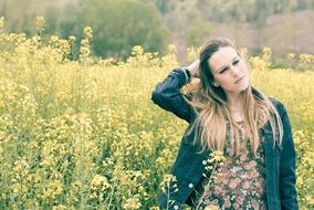 Posing blonde girl among the beautiful yellow flowers on the field