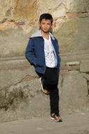 boy stands against a stone wall