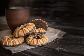 Beautiful and colorful cookies, near the drink in the brown cup, on the cloth, on the wooden surface