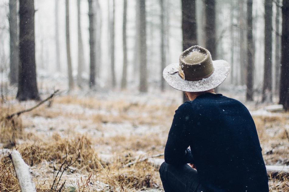 man in wide hat sits on frosted grass in forests