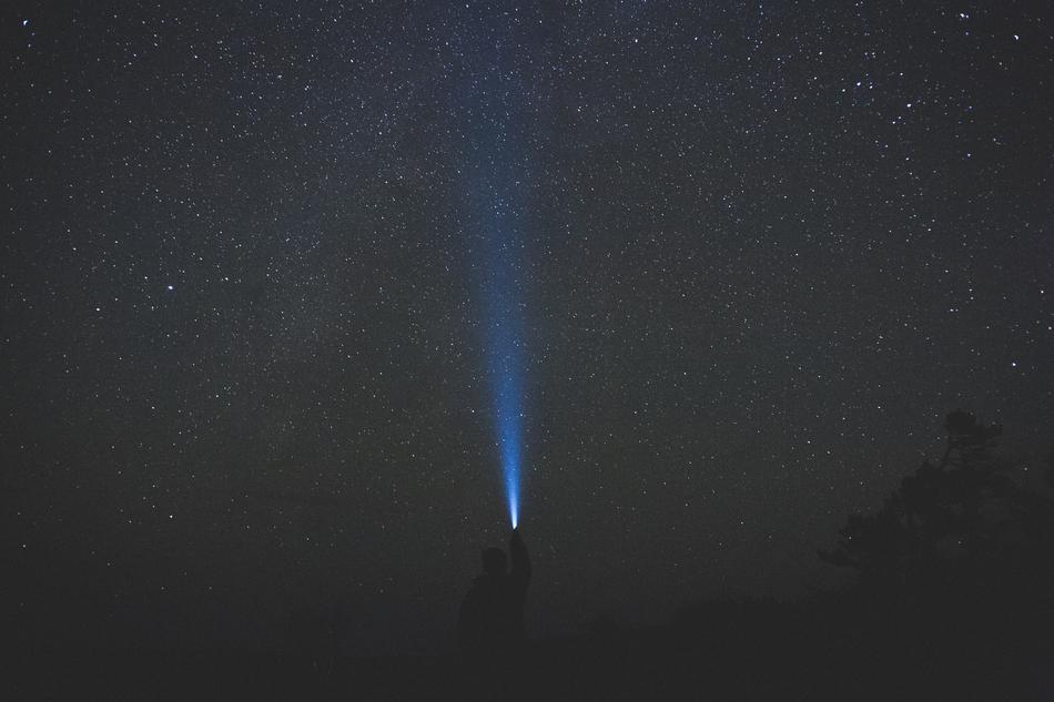 man shines a flashlight on the starry sky