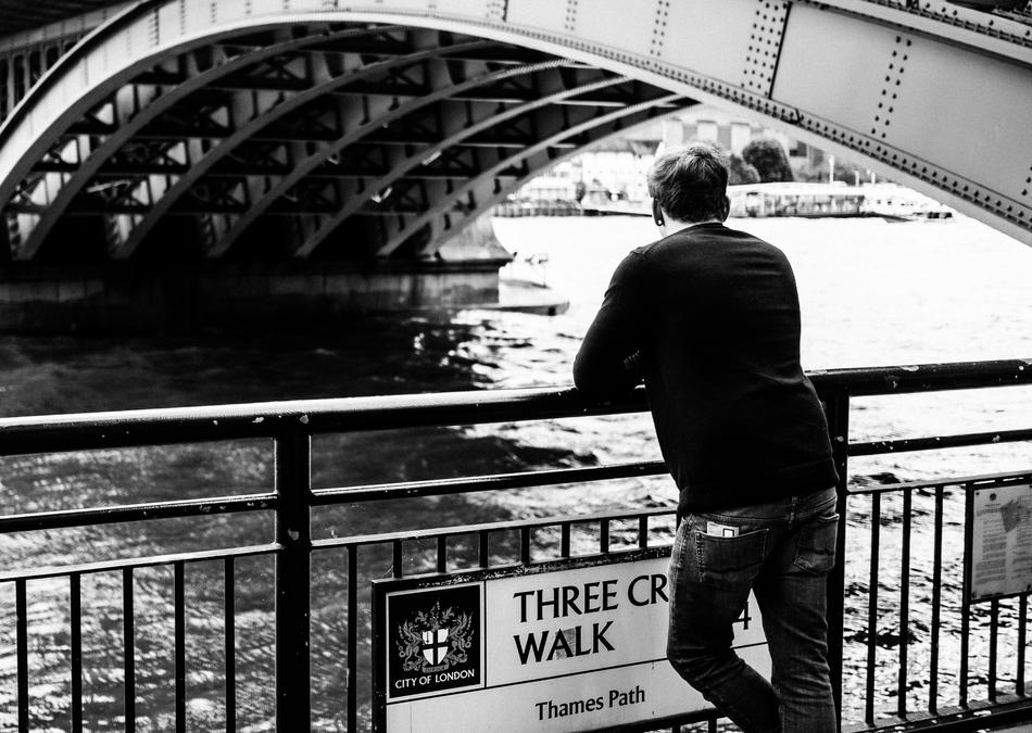 Man stands on embankment at fence near bridge