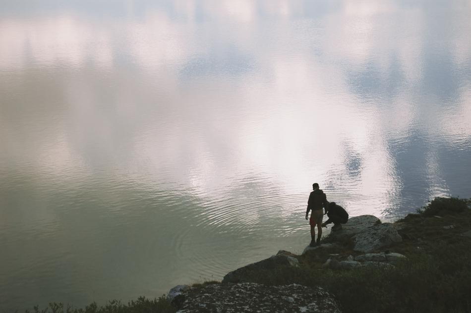 silhouette of two people on boulders by the lake