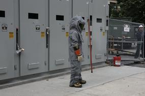 Person in bomb suit, near the worker, behind the fence