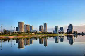 reflection of skyscrapers and a bridge in a park lake