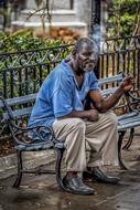 black man smokes a cigar on a bench on a street in Cuba