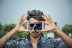 Skull image on screen of smartphone in front of young Man face