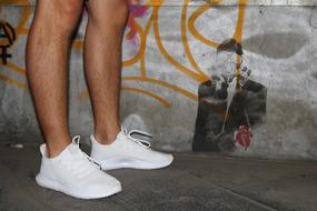 Men feet in white sneakers against a background of graffiti