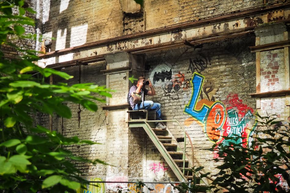 Photographer sits on external stairway at wall of abandoned building