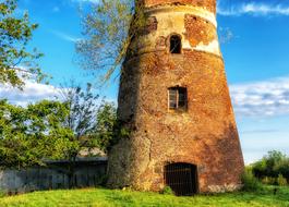 Old, colorful brick tower, among the beautiful and colorful plants, under the blue sky with clouds