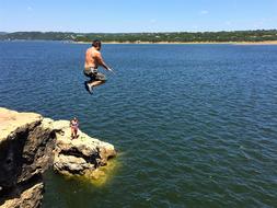 man jumps from cliff to water
