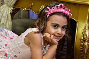 Cute girl in a princess costume and with pink crown on a background of a carriage