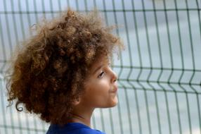 Profile portrait of a curly boy with brown hair near the fence