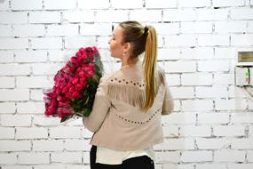 young caucasian Girl with bouquet of red roses at brick wall