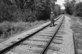 black and wite photo of Man Walking on Railroad