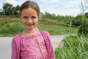 Portrait of the smiling girl, with the colorful necklaces, among the green plants, near the road