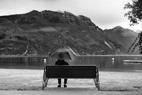 man under an umbrella on a bench near lake garda