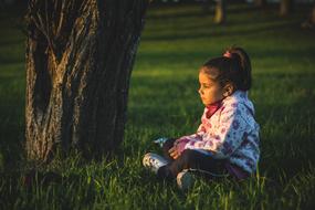 little girl on the grass near a tree at dusk