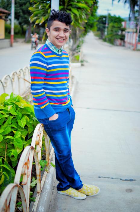 Smiling guy, posing near the fence with the green plants, on the street