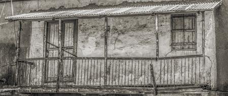 Black and white photo of the old, damaged house with the balcony and windows