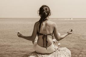 Girl sits on rock in front of sea