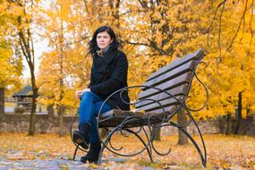 brunette Girl sits on bench in park at Autumn