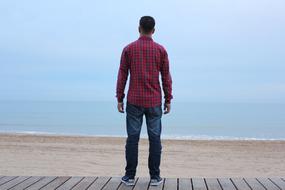 a man in a red shirt stands on a wooden deck on the beach