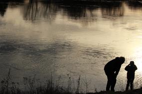 black silhouettes of father and son near the river at dusk