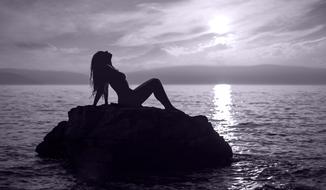 silhouette of a girl sitting on a stone in the ocean