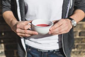 Man with watch, holding white cup of purple drink in the hands